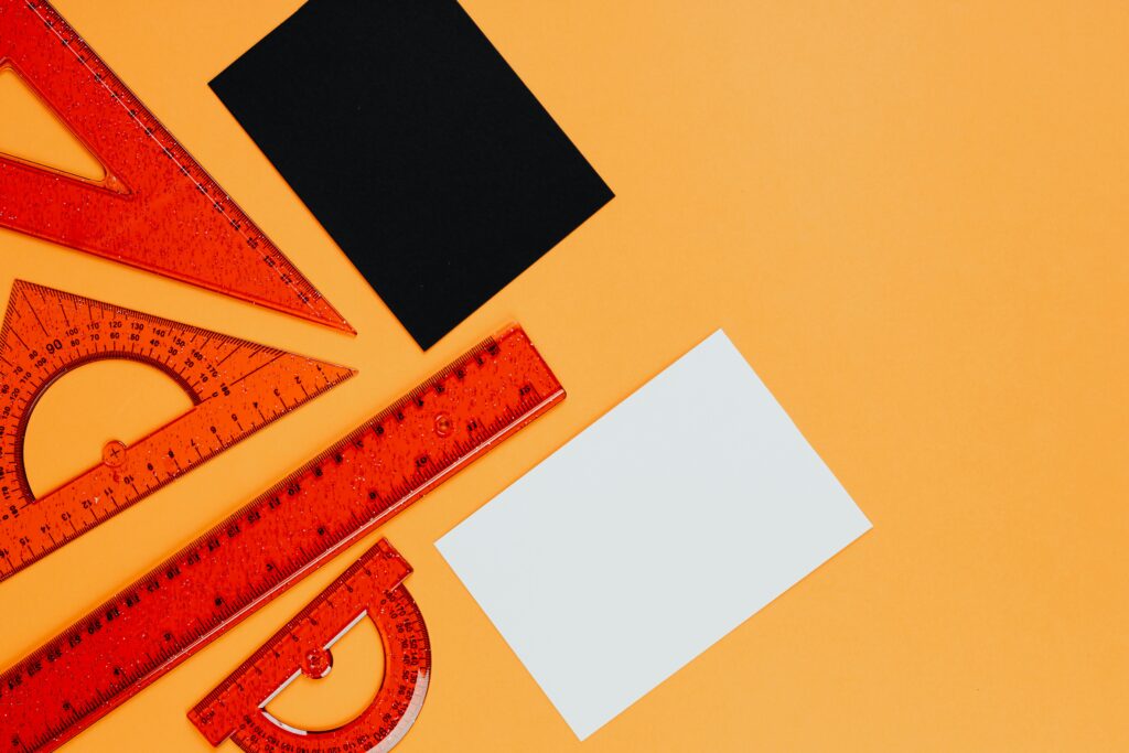 Vibrant orange rulers and geometric tools on an orange background with black and white cards.
